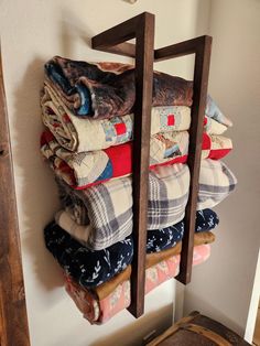 a stack of folded clothes hanging on a wall next to a wooden rack filled with blankets