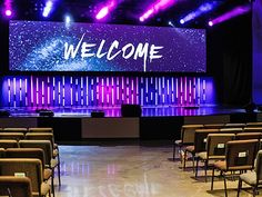 an empty stage with chairs in front of it and a welcome sign on the wall