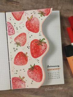 an open notebook with strawberries on it next to markers and marker pens, along with a calendar