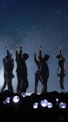 five people standing on top of a hill with their hands in the air and lights shining behind them