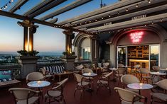 an outdoor dining area with tables and chairs overlooking the city at sunset or dawn,