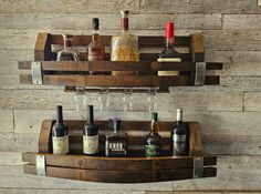 two wooden shelves holding bottles and glasses on top of each other in front of a wood wall