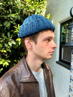 a man wearing a blue knitted hat standing in front of a wall with a birdcage