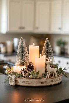 Festive centerpiece with lit candles, miniature snowy trees, and a reindeer figurine. Rustic Winter Table Decor, Open Shelf Christmas Decor Kitchen, Cozy Christmas Decor Kitchen, Christmas Home Decor Kitchen, Coffee Table Centerpieces Christmas, Christmas Decorative Tray, Christmas Centerpiece For Island, Kitchen Corner Counter Christmas Decor Ideas, Christmas Coffee Table Tray Decor