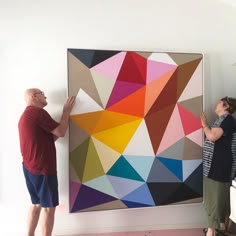 two people standing next to a large colorful painting