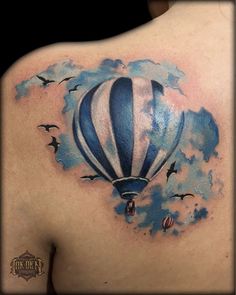 a watercolor hot air balloon tattoo on the back of a man's shoulder