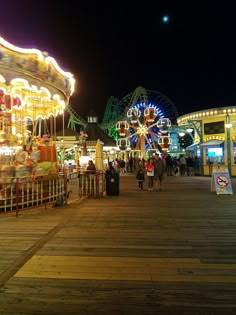 an amusement park at night with people on the boardwalk and carousels in the background