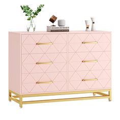 a pink dresser with gold handles and some plants on the top, against a white background