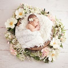 a baby is sleeping in a basket surrounded by flowers and feathers on a white wooden floor