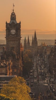 the sun is setting over an old city with tall buildings and a clock tower in the distance