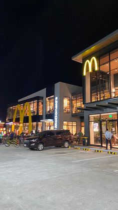 a mcdonald's restaurant is lit up at night with people walking in the parking lot