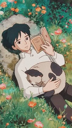 a man sitting in the grass reading a book while holding a cat on his lap