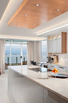 a large kitchen with an island counter top and white cabinets next to a window overlooking the ocean