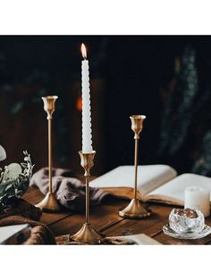 three candles sitting on top of a wooden table next to an open book and glass vase