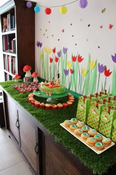 a table filled with cupcakes and cakes on top of green grass covered trays