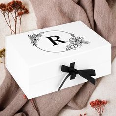 a white box with a black ribbon around it and some flowers on the ground next to it