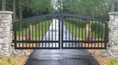 an iron gate with stone pillars leading to a driveway