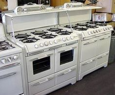 several white stoves and ovens are on display in a room with other appliances