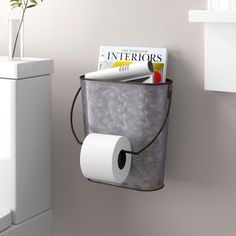 a toilet paper holder hanging on the wall next to a trash can with magazines in it