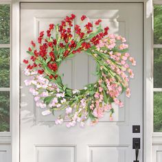 a wreath is hanging on the front door with red and pink flowers in it's center