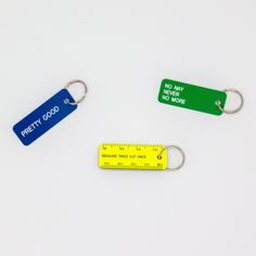 three different colored plastic keychains on a white surface, one with a measuring tape