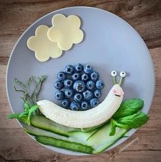 a plate with blueberries, cucumbers and a banana on it that looks like a snail