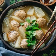 a bowl filled with meatballs and vegetables next to chopsticks on a table