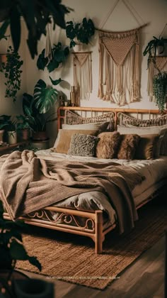 a bed with lots of pillows and blankets on it in a room filled with potted plants