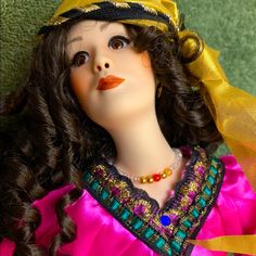 a close up of a doll wearing a yellow hat and pink dress with gold trim