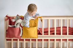 a baby in a crib playing with stuffed animals and fabric storage bags on the bed