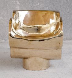 a gold colored metal bowl sitting on top of a wooden stand next to a wall