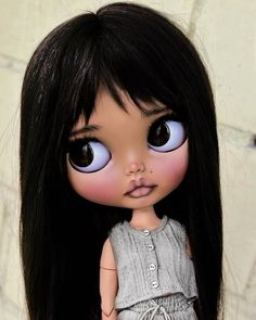 a close up of a doll with long black hair and blue eyes wearing a gray dress