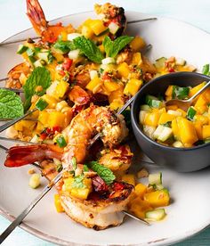 a white plate topped with shrimp and mango salad next to a bowl of salsa dressing