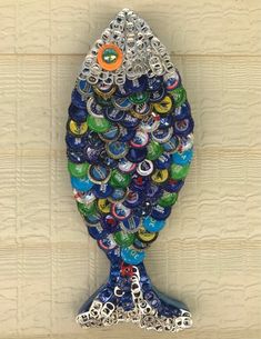 a bottle cap fish made out of beer caps on a wooden wall with chains hanging from it's sides