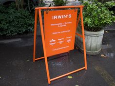 an orange sign sitting on the side of a road next to potted planters