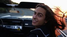 a man with long hair sitting in the driver's seat of a car smiling