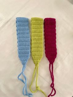 three crocheted headbands are lined up on a white tablecloth, one is blue and the other is pink