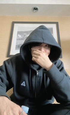 a man in a black hoodie sitting down with his hands on his face and looking at the camera