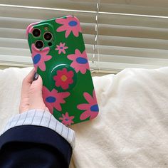 a person is holding a phone case with pink flowers on it, in front of a window