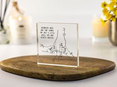 a glass block with a drawing on it sitting on top of a wooden tray next to some yellow flowers