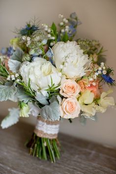 a bouquet of white and peach flowers on a wooden table with greenery around it