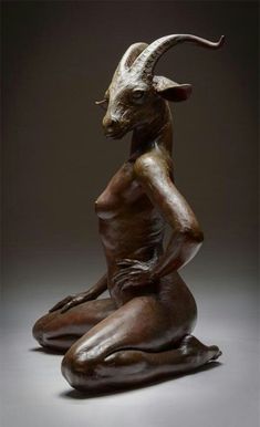 a statue of a woman with horns sitting on the ground in front of a dark background