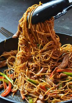 noodles being cooked in a skillet with tongs and fork sticking out of it