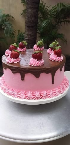 a pink cake with chocolate icing and strawberries on top sitting on a table