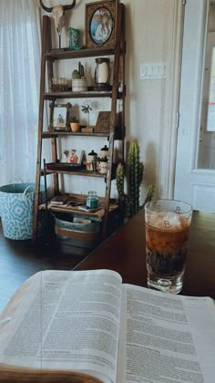 an open book sitting on top of a wooden table next to a tall shelf filled with books