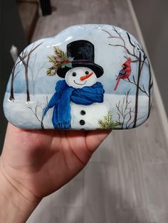 a hand holding a painted rock with a snowman on it