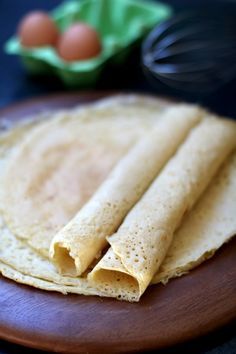 three tortillas on a wooden plate next to eggs