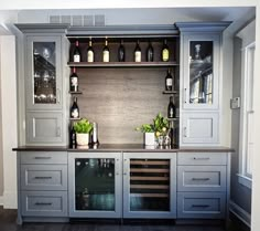 a kitchen with grey cabinets and wine bottles on the counter top, along with two vases filled with green plants