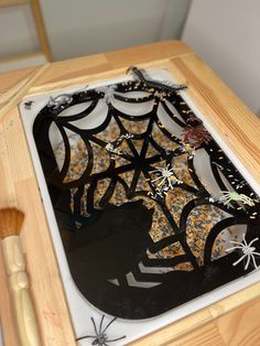 a wooden table topped with a spider web cut out of paper next to a brush