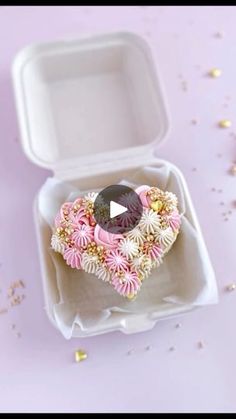 an open box with a ring inside on a pink surface next to confetti and sprinkles